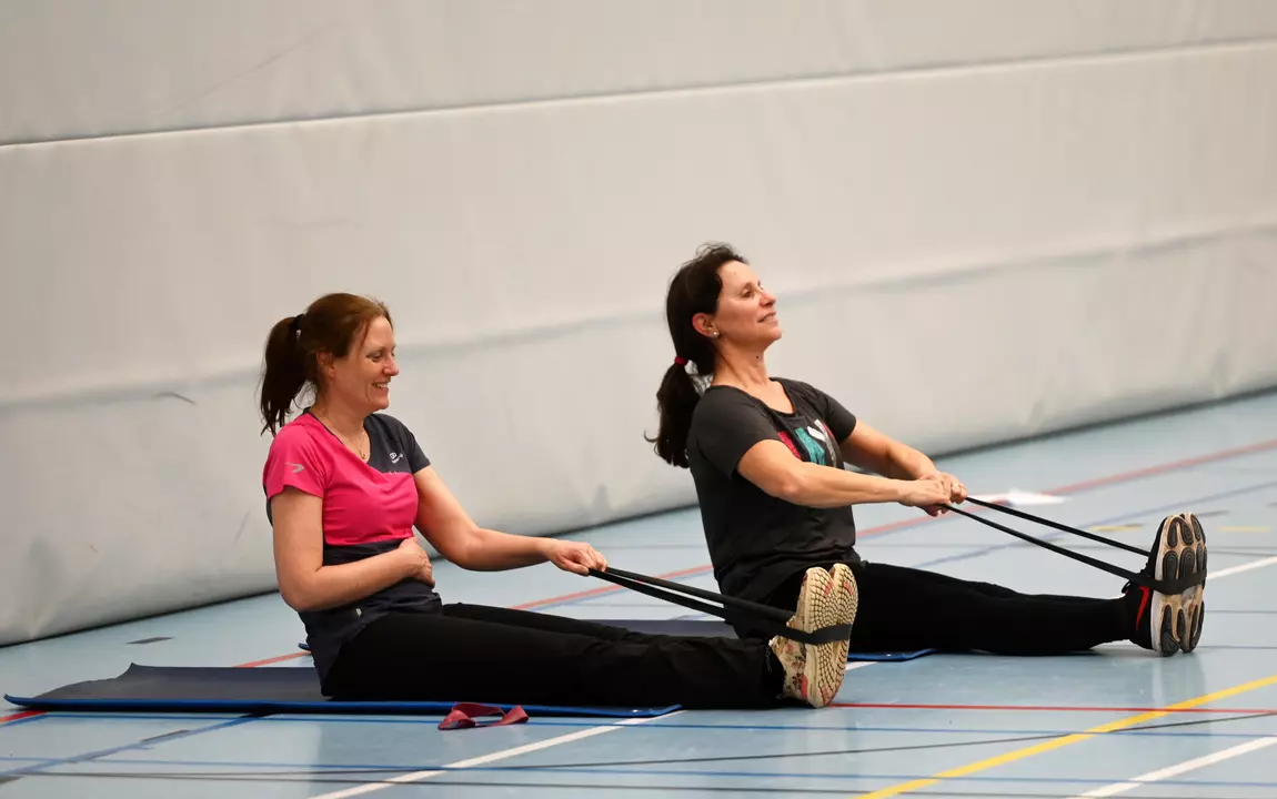 Twee dames die al zittend stretchoefeningen doen met een rekker
