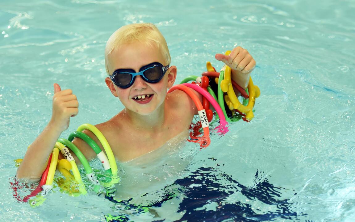Vrolijk kindje in het zwembad met ringen rond zijn arm