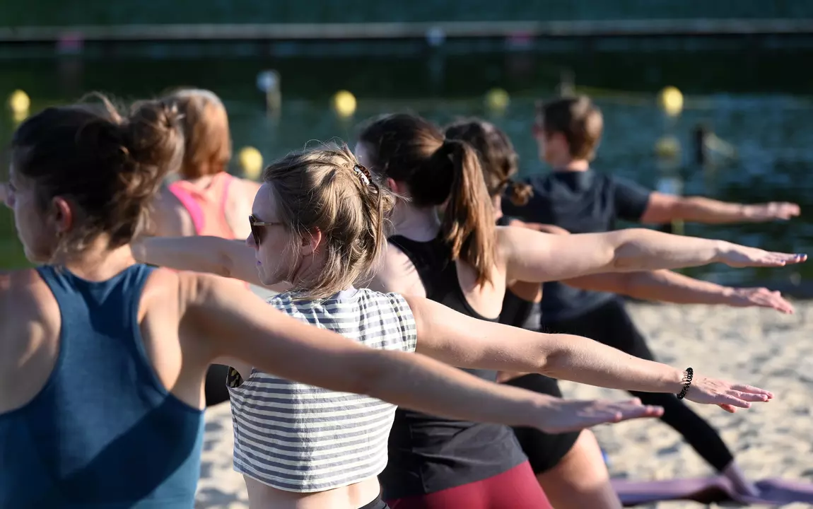 Sporters die tijdens de zomersport summer yoga beoefenen op het strand van de Blaarmeersen