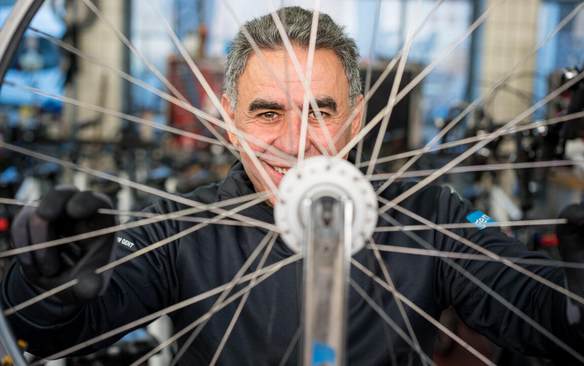 close-up van lachende man die doorheen de spaken van een fiets kijkt