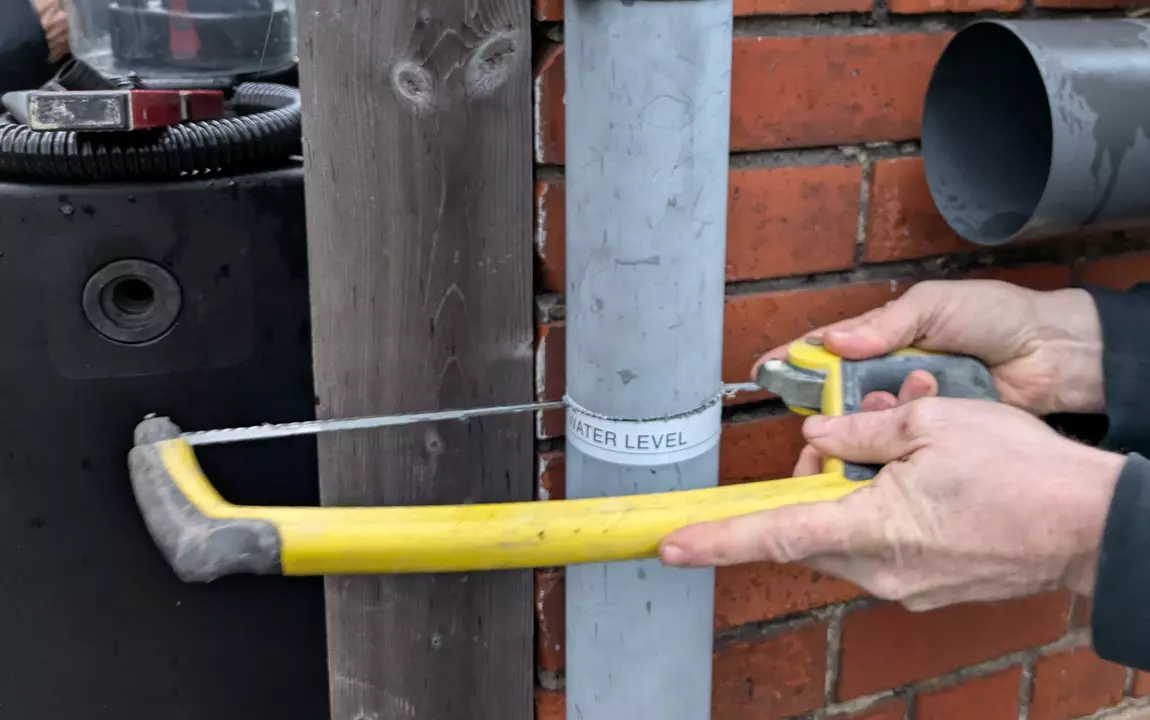 Man zaagt een regenpijp door om een regenwaterton te koppelen