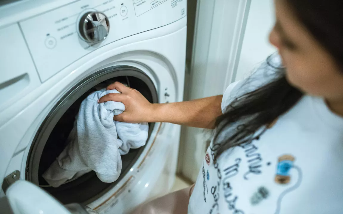Vrouw steekt kleren in een wasmachine