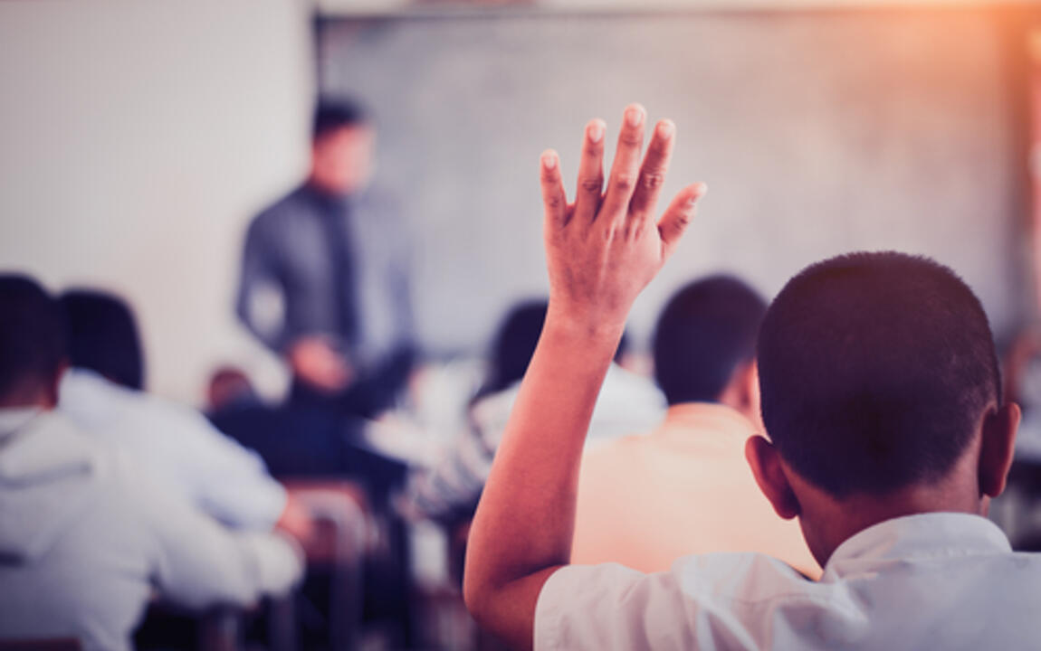 Foto van kind dat hand opsteekt in de klas