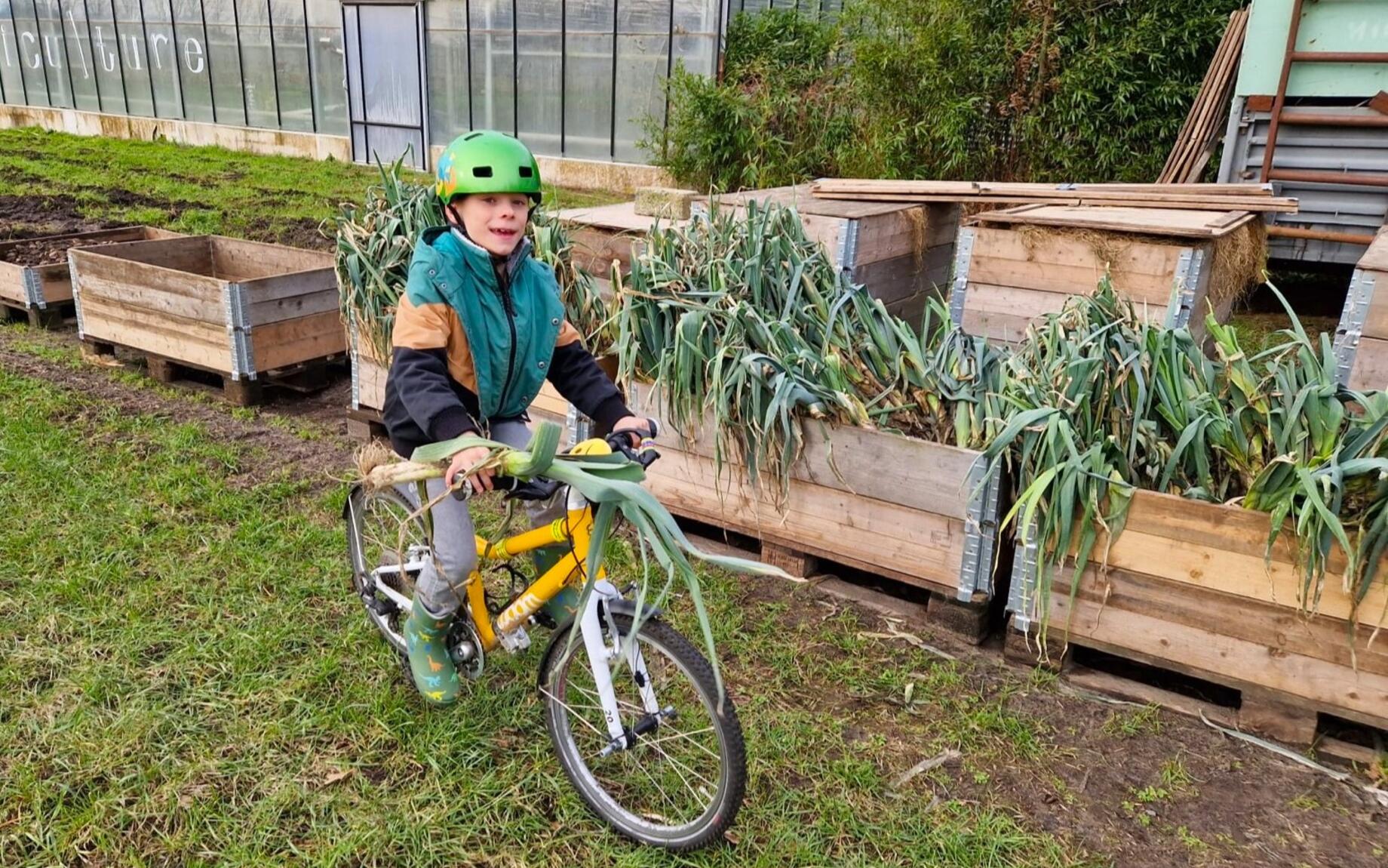 Kind op fiets met prei in zelfoogsboerderij