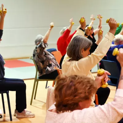 Senioren die met gewichtjes in de hand de armen strekken tijdens stoelgymnastiek