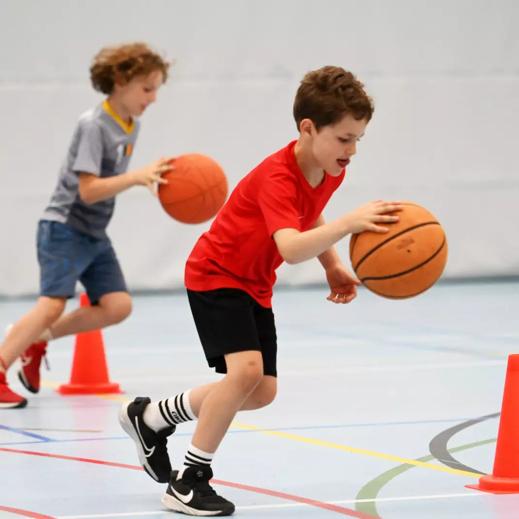 Twee jongens die met een basketbal aan het dribbelen zijn