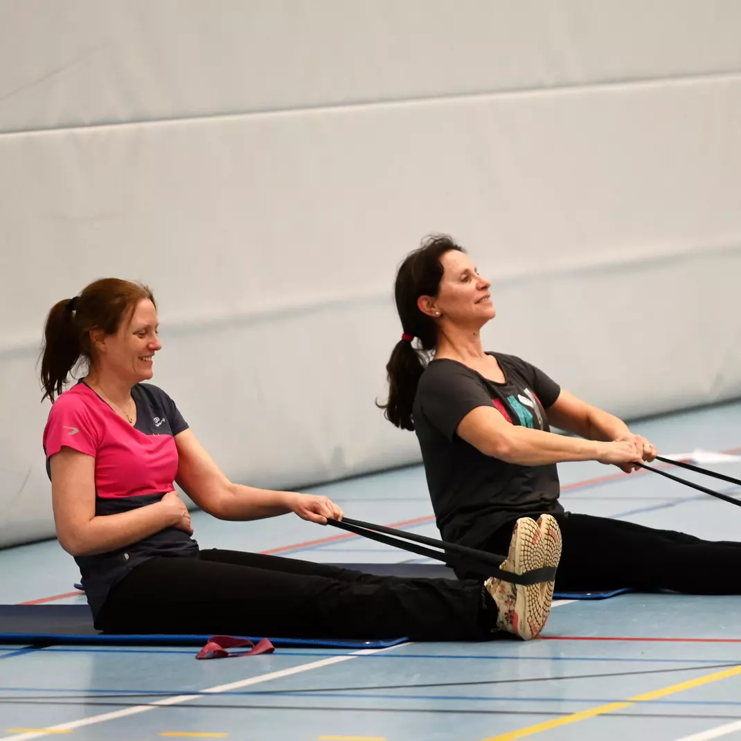 2 dames die in zit stretchen met een dynaband tijdens de les fitmix