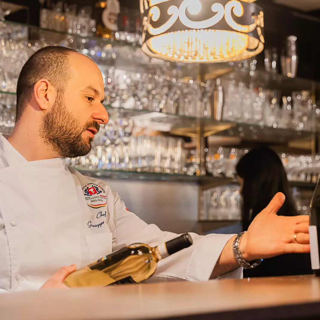 Ober restaurant Firenze staat achter de bar met fles wijn in de hand