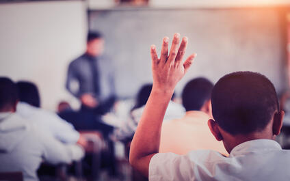 Foto van kind dat hand opsteekt in de klas