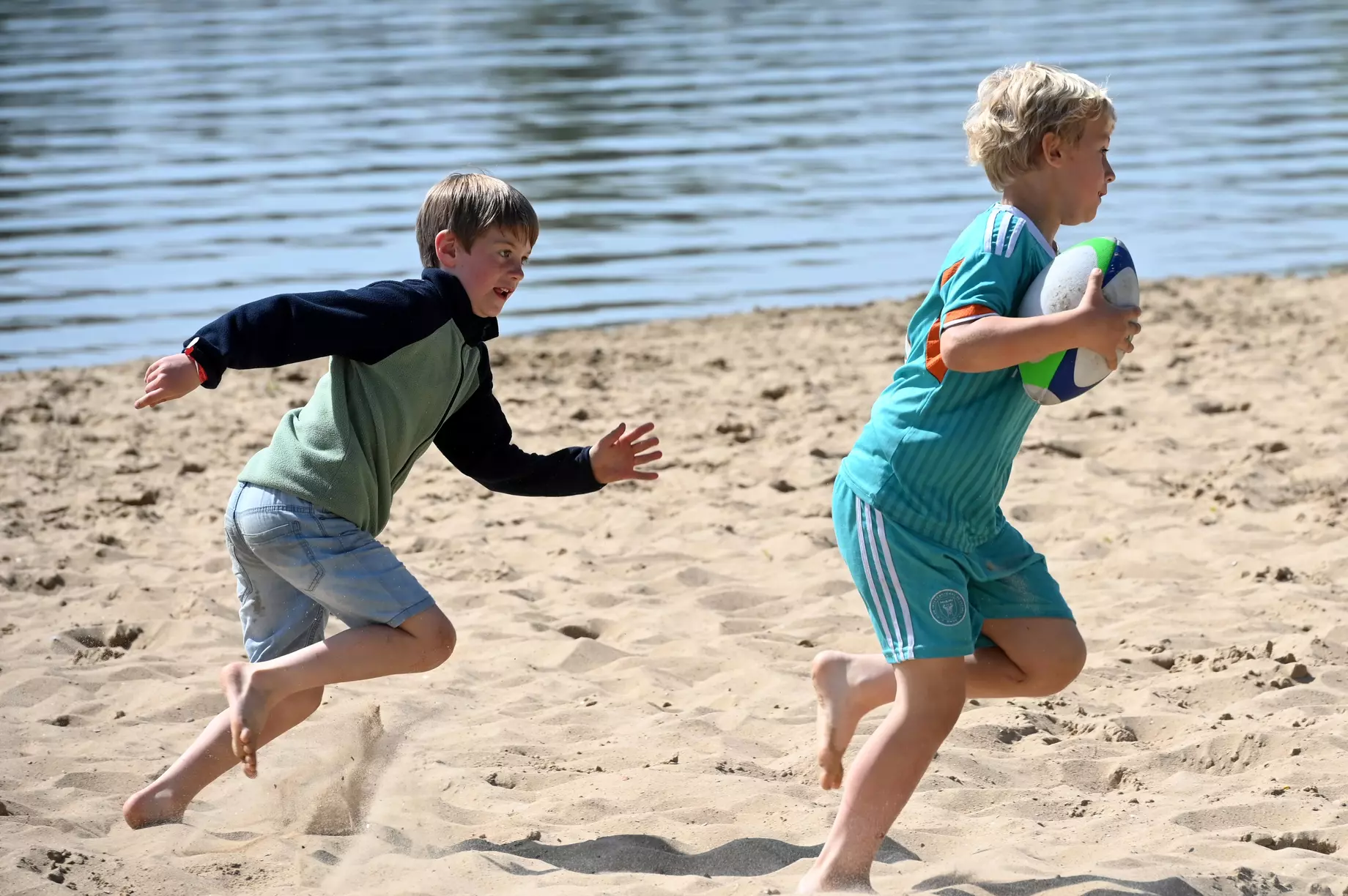 Twee kinderen die tijdens een sportkamp mekaar nazitten op het strand van de Blaarmeersen